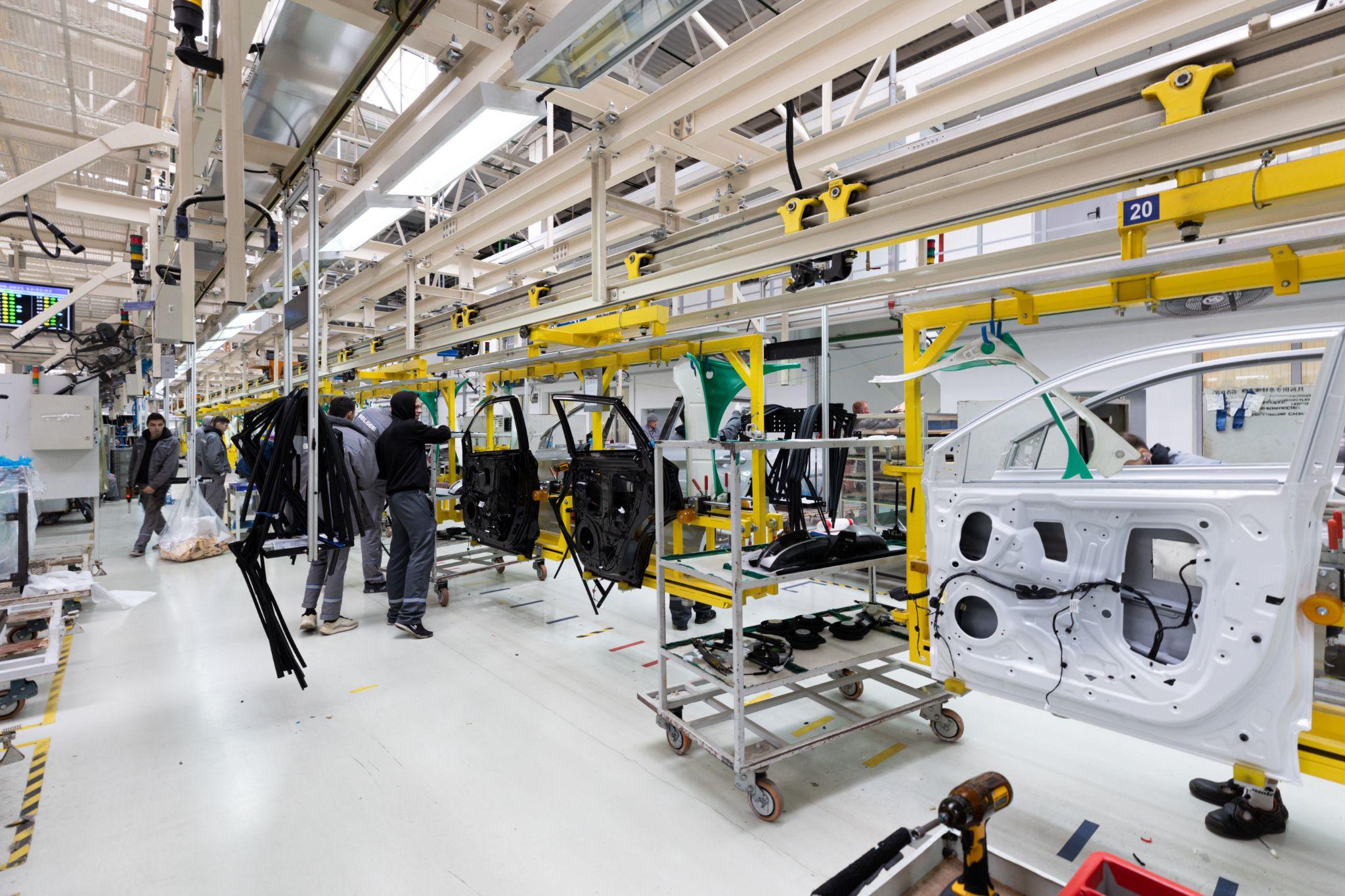 Workers on an automotive assembly line install door components on vehicles moving through a factory.