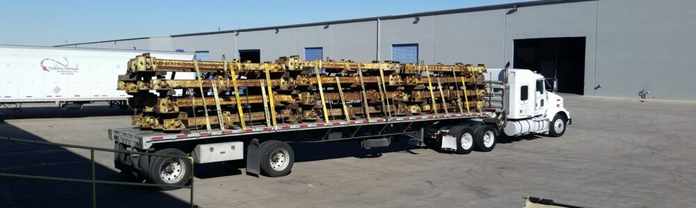 A flatbed truck loaded with freight parked outside a distribution facility.